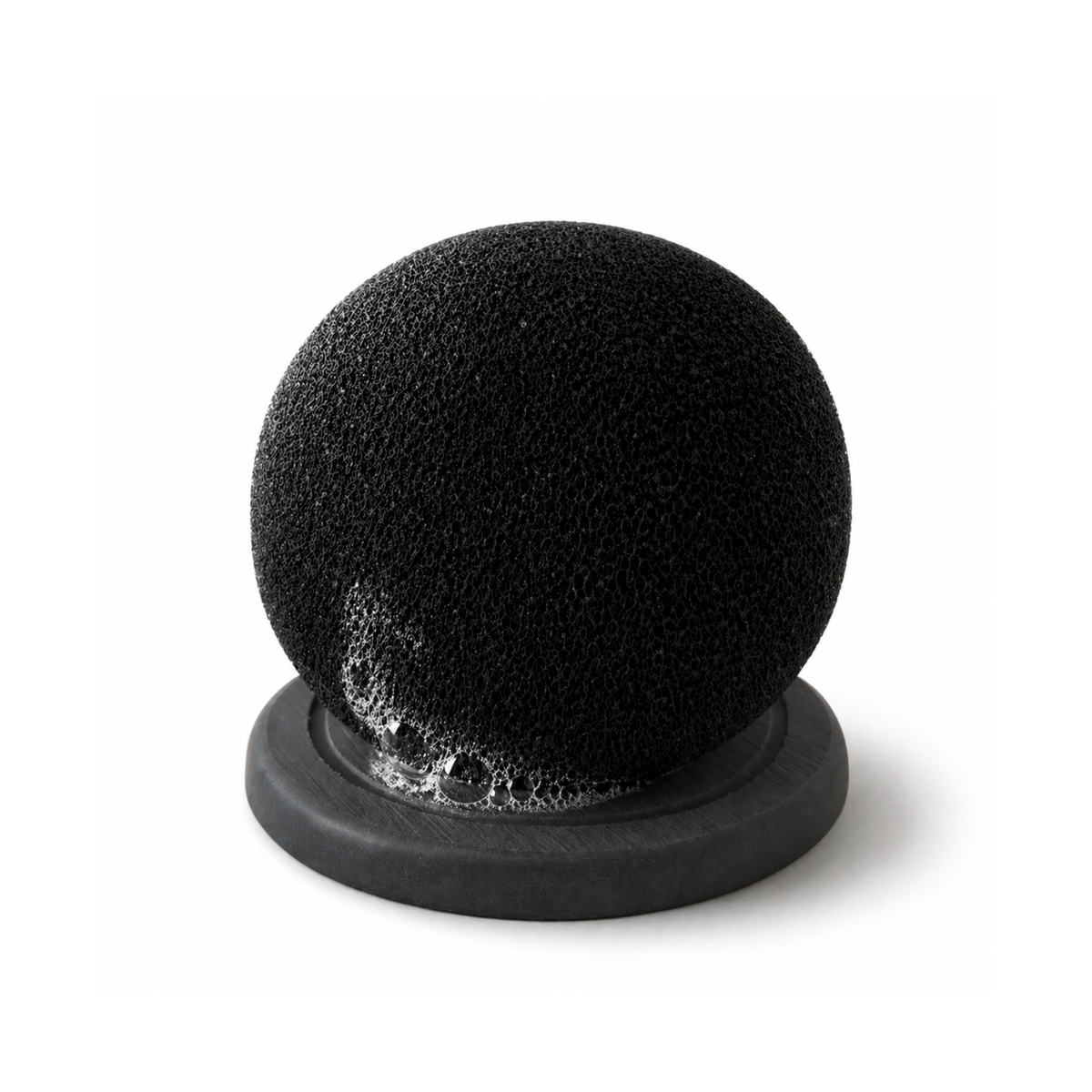 Black spherical ORB Sponge with soap suds resting on its drying base.
